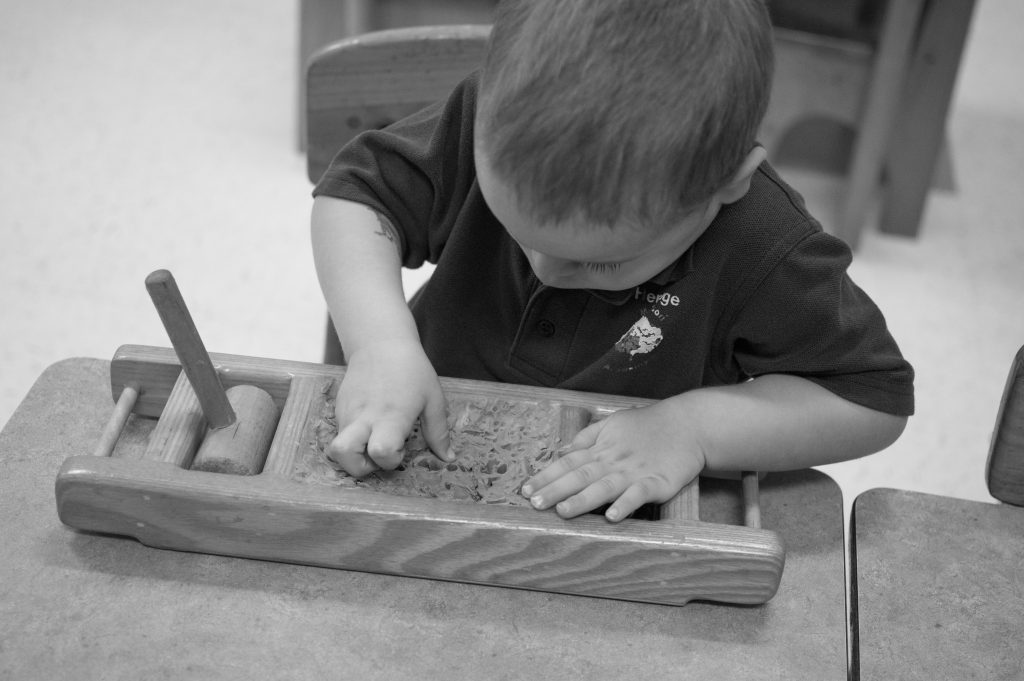 A child's hands working a wooden Montessori material at a low table