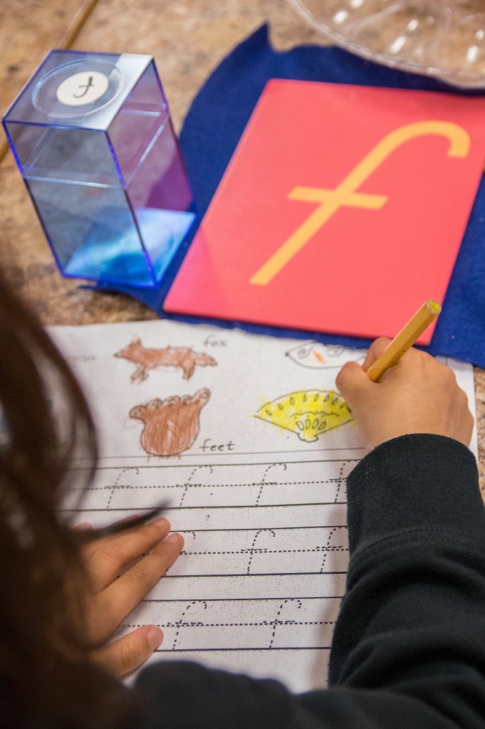 A child practicing letters at a Primary-room writing table